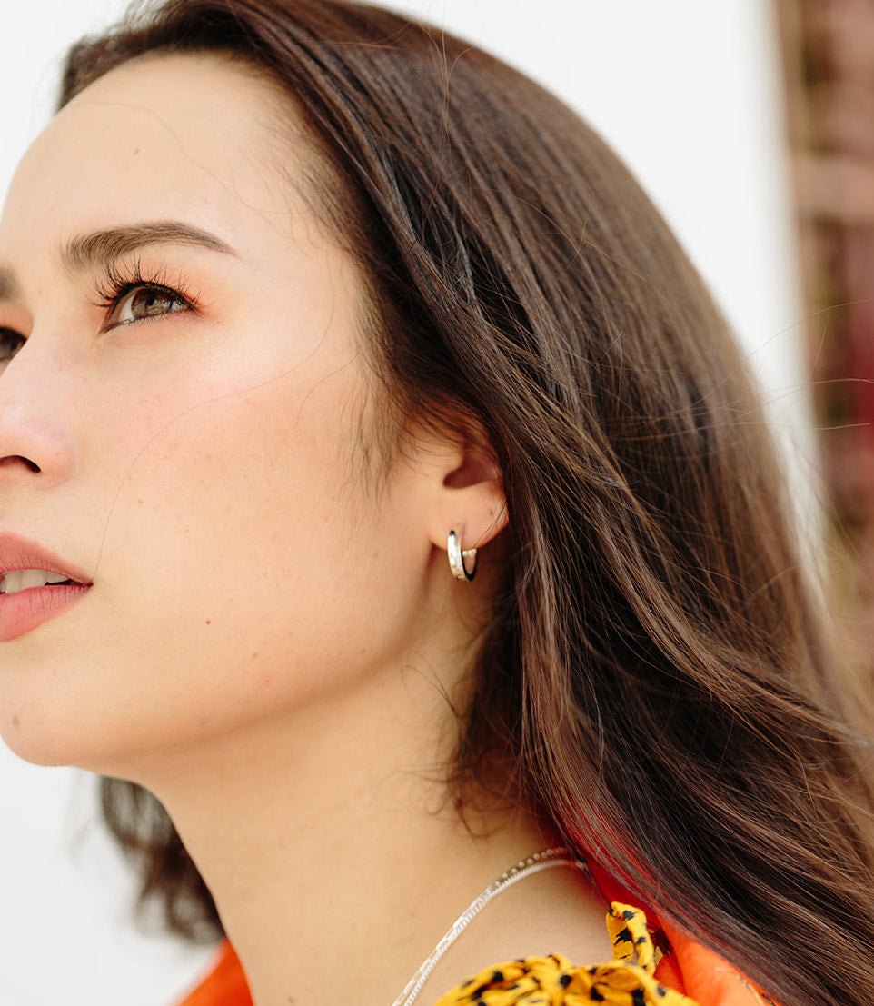 an asian model looking up wearing sterling silver huggie earrings with brown hair