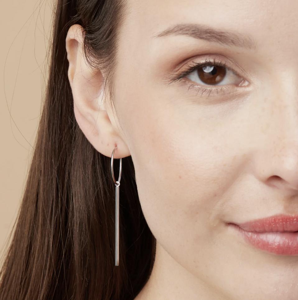 a model with brown hair wearing wire hoops in sterling silver with beige color background