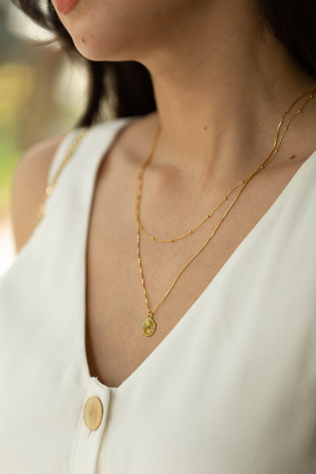 a model wearing a white dress and two 14k gold plated necklaces layered