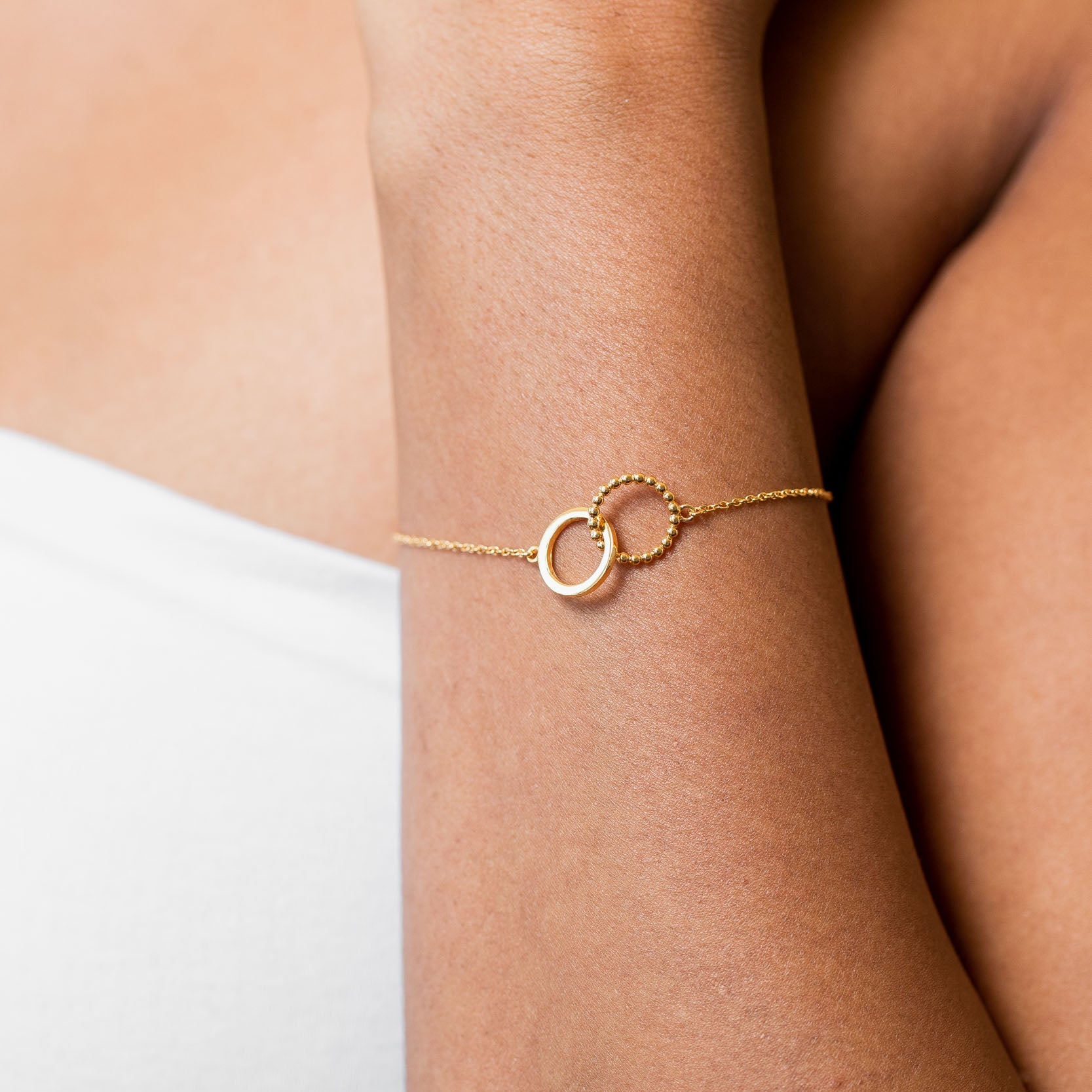a model with tan skin wearing a 14k gold vermeil bracelet with interlocking circles and white top