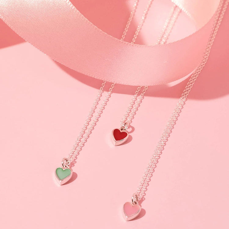three sterling silver heart pendant necklaces with red, green, and pink stones with a soft pink ribbon on a soft pink color background