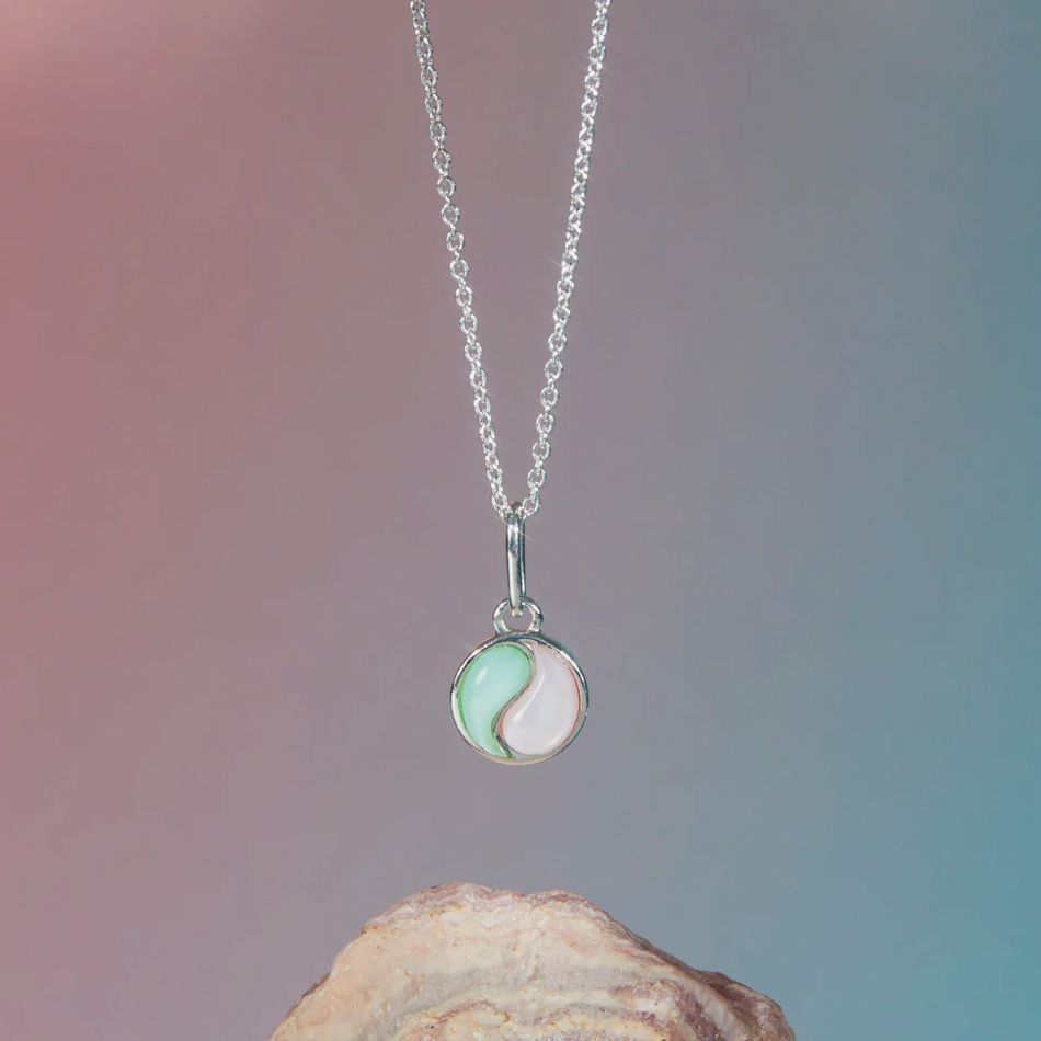 Sterling silver necklace with a yin yang pendant featuring a mint green and soft pink design, displayed against a gradient background with a rock at the base.