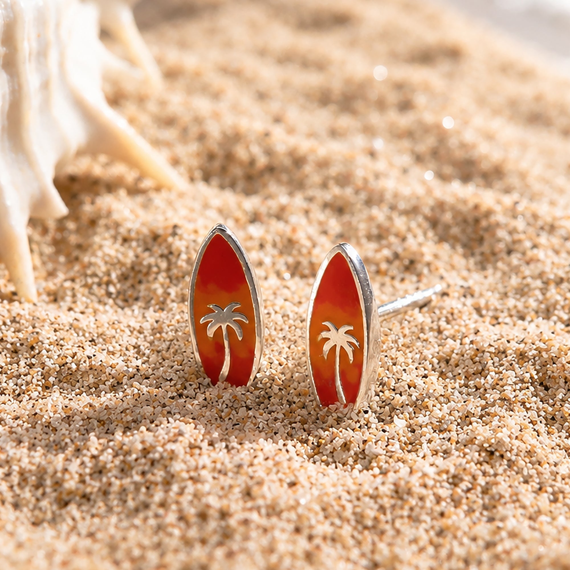 Boma Jewelry Surfboard-shaped earrings with palm tree design on a sandy surface
