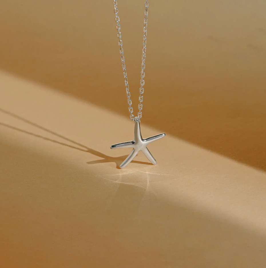 A starfish sterling silver pendant necklace displayed against a beige paper background with gentle, soft lighting