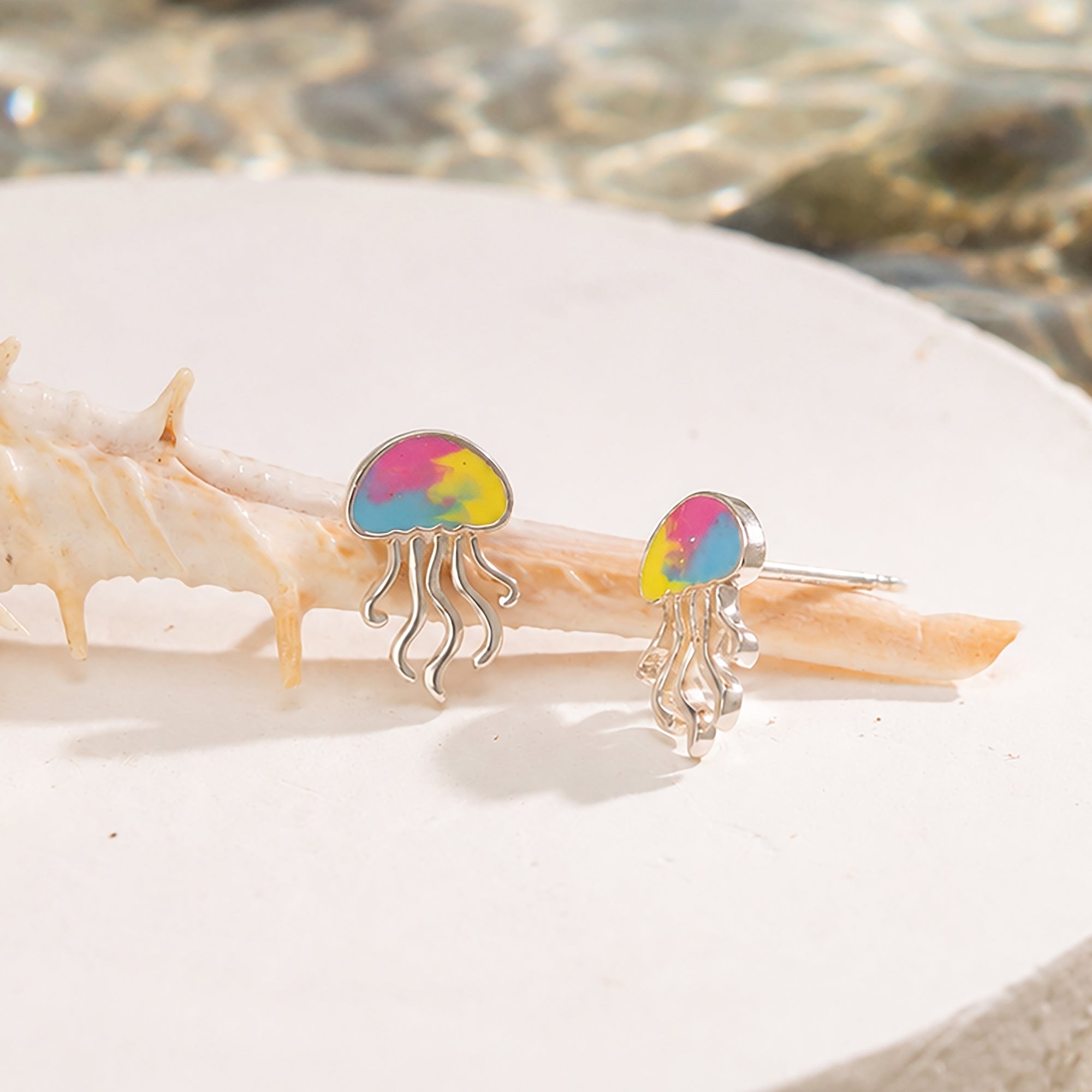 Jellyfish-shaped earrings with colorful designs on a shell.