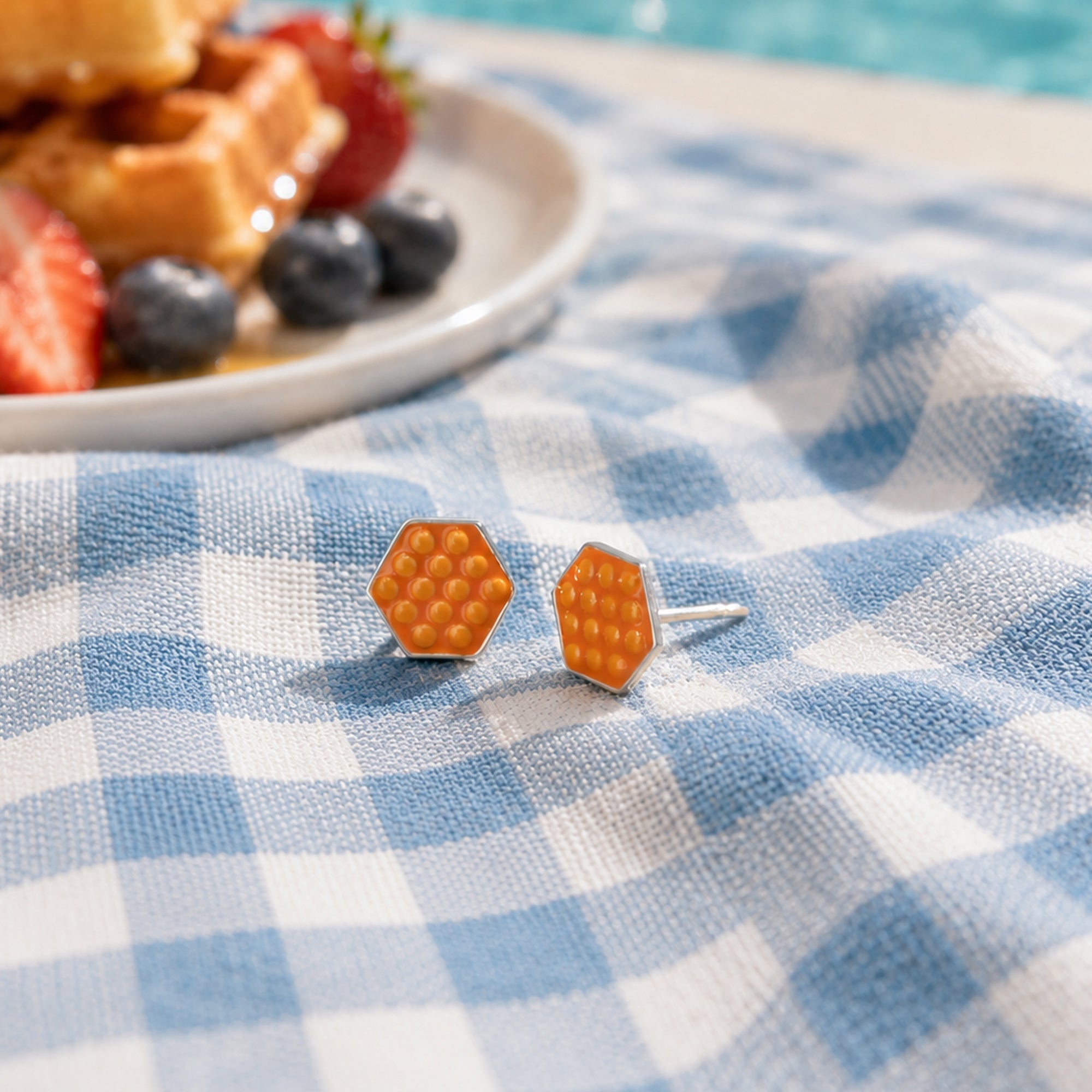 Hexagonal earrings on a blue and white checkered tablecloth with waffles and berries in the background.