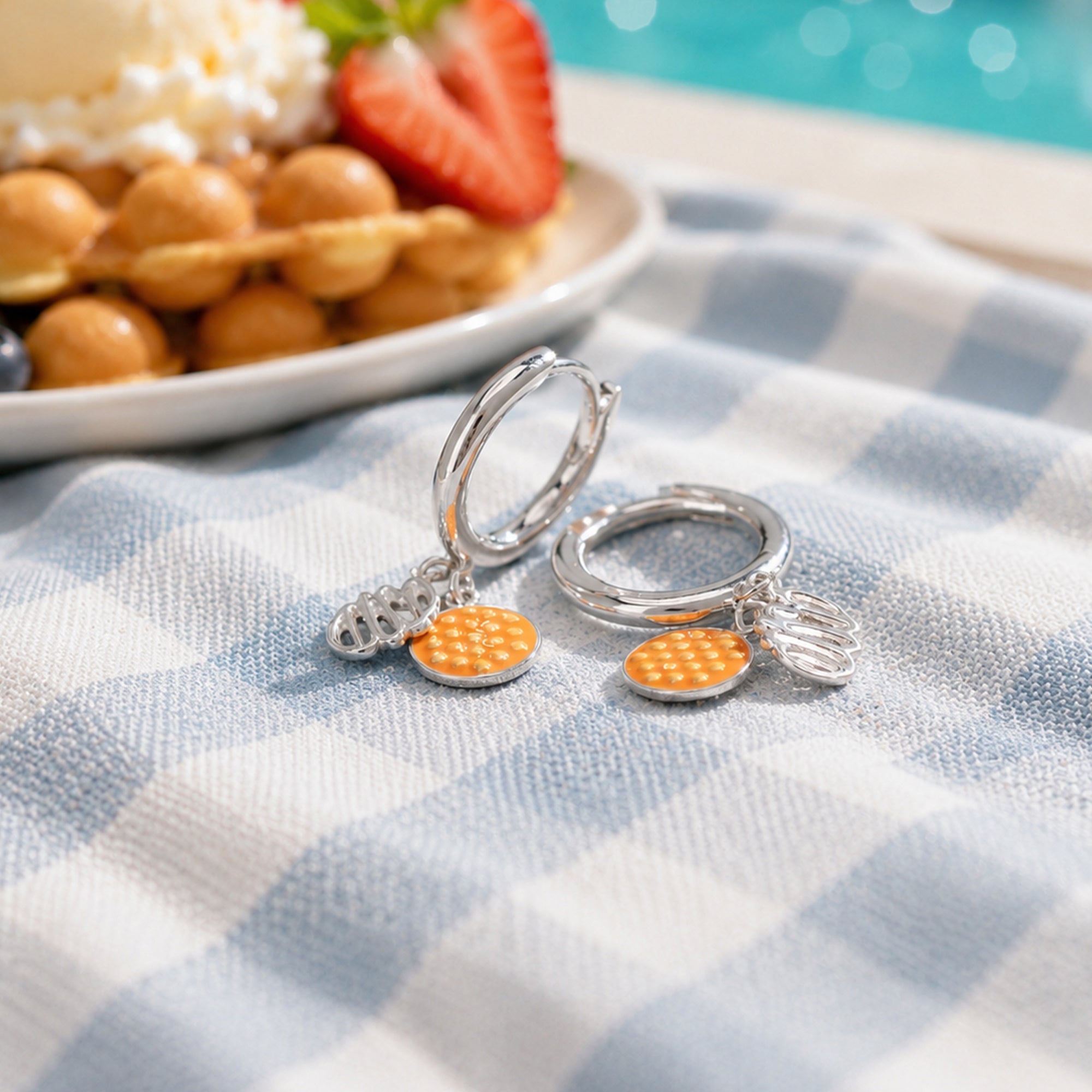 Silver keychains with orange charms on a checkered tablecloth with pastries in the background
